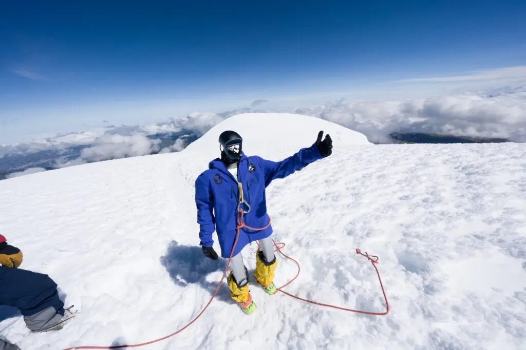 A Unitree G1 humanoid in a blue jacket on a snowy summit above the clouds